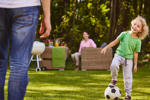 Child plays soccer with his dad on artificial grass in the backyard